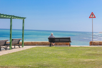 Man sitting on bench overlooking sea, Praia da Luz Beach, Lagos, Algarve, Portugal