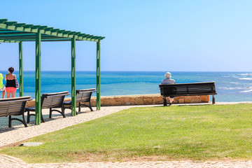 Man sitting on bench overlooking sea, Praia da Luz Beach, Lagos, Algarve, Portugal