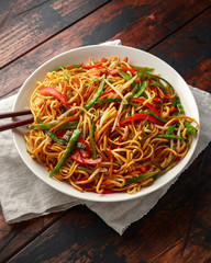 Chow mein, noodles and vegetables dish with wooden chopsticks