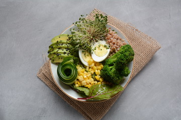 Green vegetarian buddha bowl lunch with boiled egg, avocado, corn, arugula beet leaves,fresh cucumber, buckwheat, broccoli sprouts.Healthy vegan food concept