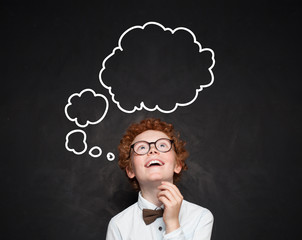 Happy smart kid with empty speech clouds bubbles at the classroom blackboard. Education and school concept. Student boy portrait