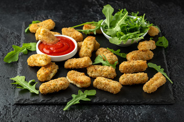 Fried mozzarella cheese sticks in breadcrumbs with ketchup sauce and wild rocket leaves