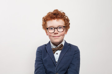Cute child in glasses and blue suit portrait. Funny redhead boy on white background