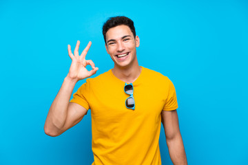 Handsome man over blue background showing ok sign with fingers