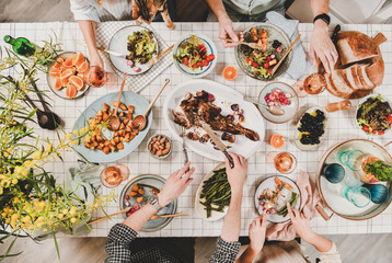 Family or friends gathering dinner. Flat-lay of peoples hands with roasted lamb shoulder, salads,...
