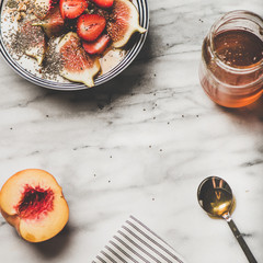 Healthy breakfast. Flat-lay of Greek yogurt granola bowl with strawberry, figs, peach, chia seeds and honey over marble background, top view, copy space, square crop. Vegetarian, dieting food concept