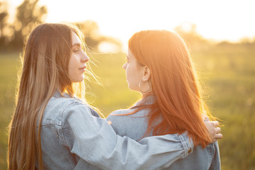 Two girls standing together under sunset. Best friends.