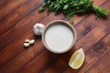 Tahini sauce made from sesame seeds in bowl with parsley on wooden background