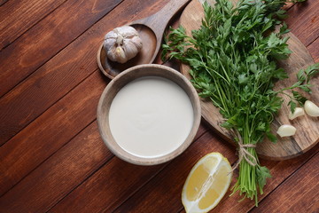 Tahini sauce made from sesame seeds in bowl with parsley on wooden background