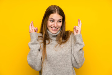 Young woman with long hair over yellow background with fingers crossing