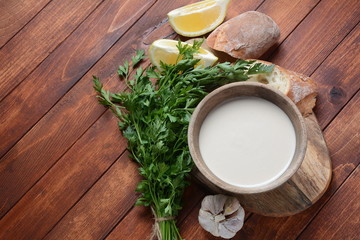 Tahini sauce made from sesame seeds in bowl with parsley on wooden background