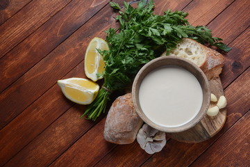 Tahini sauce made from sesame seeds in bowl with parsley on wooden background