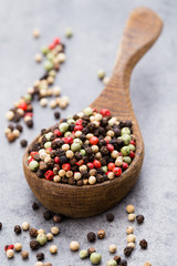 Peppercorn mix in a wooden bowl on grey table.