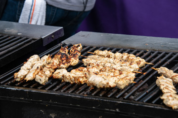 Large open outdoor barbecue grill cooking kabob made of chunks of chicken on wooden skewers.