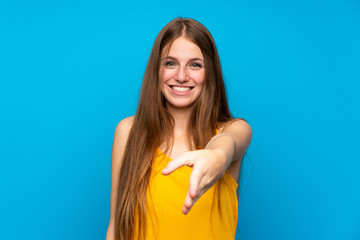 Young woman with long hair over isolated blue wall shaking hands for closing a good deal