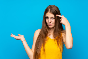 Young woman with long hair over isolated blue wall making the gesture of madness putting finger on...