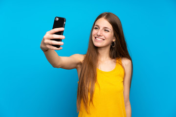 Young woman with long hair over isolated blue wall making a selfie