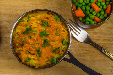 Shepherds or cottage pie in serving dish with parsley on wooden board.