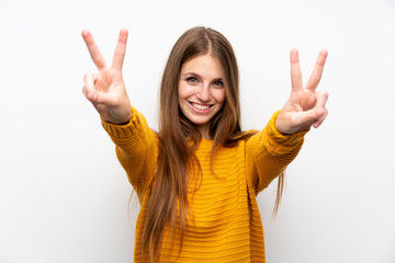 Young woman with yellow over isolated white wall smiling and showing victory sign