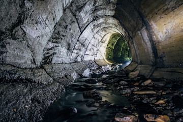 Naklejka premium Underground river flowing through large oviform underground turning drainage sewer tunnel