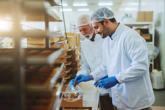 Two hard working food plant employees in sterile uniforms packing cookies in boxes.