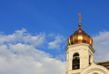 Church golden dome and bell tower with cross on blue sky background 