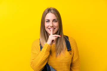 Woman with overalls over isolated yellow wall doing silence gesture