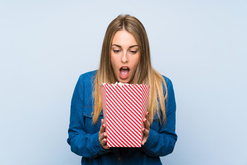 Obraz premium Blonde woman with popcorns over blue wall doing surprise gesture