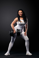 Fototapeta na wymiar Size plus woman sporty fit woman in white sportswear, athlete with dumbbells makes fitness exercising on black background with lights. Motivation for fat people.