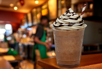 Cup of frappuccino coffee with cream and chocolate sauce on wooden counter at cafe.