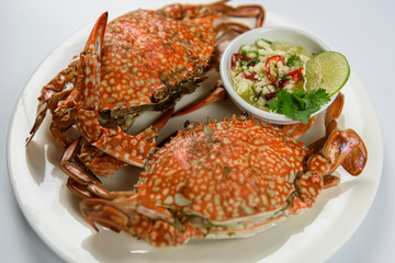 Steamed blue crab on white plate with spicy seafood sauce