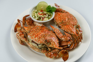 Steamed blue crab on white plate with spicy seafood sauce