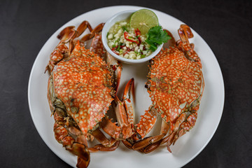 Steamed blue crab on white plate with spicy seafood sauce