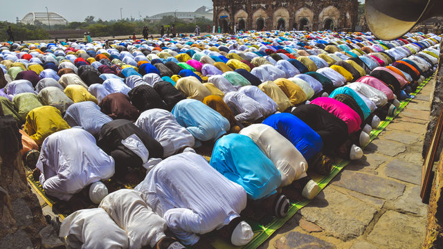 A gathering of Muslim men and children bowing down and offering Namaz prayers on the occasion of Eid'Al-Fitr 2019. They are dressed in kurta pyjamas of many colours, and wearing traditional skullcaps