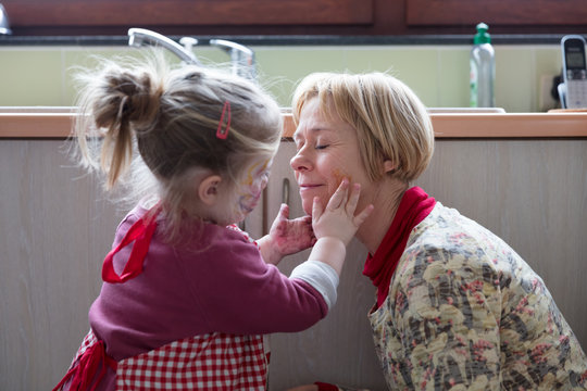 Little girl painting on her grandmothers' face with fingers