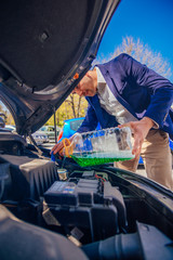 Handsome entrepreneur business casually dresses is pouring some antifreeze in his car's engine.