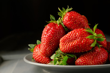A pile of strawberries in a gray plate on a gray wooden table on a black background