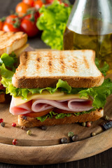 Close-up photo of a club sandwich. Sandwich with meat, prosciutto, salami, salad, vegetables, lettuce, tomato, onion and mustard on a fresh sliced rye bread on wooden background. Olives background.