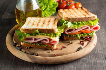 Close-up photo of a club sandwich. Sandwich with meat, prosciutto, salami, salad, vegetables, lettuce, tomato, onion and mustard on a fresh sliced rye bread on wooden background. Olives background.