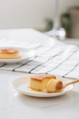 Woman's hand cutting homemade caramel custard pudding on white plate. Over white table with napkin.