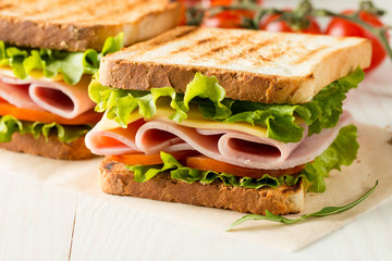 Close-up photo of a club sandwich. Sandwich with meat, prosciutto, salami, salad, vegetables, lettuce, tomato, onion and mustard on a fresh sliced rye bread on wooden background. Olives background.