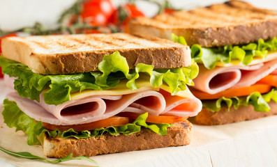 Close-up photo of a club sandwich. Sandwich with meat, prosciutto, salami, salad, vegetables, lettuce, tomato, onion and mustard on a fresh sliced rye bread on wooden background. Olives background.