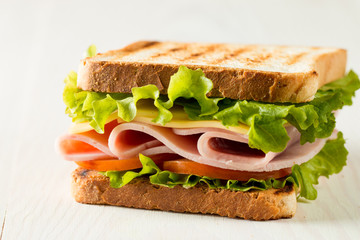 Close-up photo of a club sandwich. Sandwich with meat, prosciutto, salami, salad, vegetables, lettuce, tomato, onion and mustard on a fresh sliced rye bread on wooden background. Olives background.