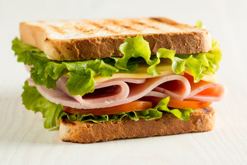 Close-up photo of a club sandwich. Sandwich with meat, prosciutto, salami, salad, vegetables, lettuce, tomato, onion and mustard on a fresh sliced rye bread on wooden background. Olives background.