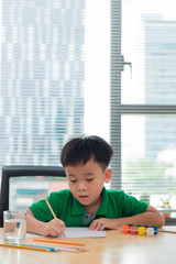 Cute boy is drawing using color pencils, isolated over white