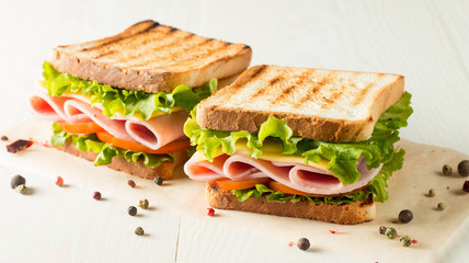 Close-up photo of a club sandwich. Sandwich with meat, prosciutto, salami, salad, vegetables, lettuce, tomato, onion and mustard on a fresh sliced rye bread on wooden background. Olives background.