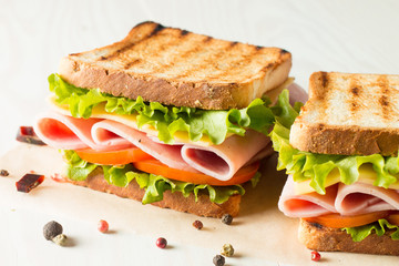 Close-up photo of a club sandwich. Sandwich with meat, prosciutto, salami, salad, vegetables, lettuce, tomato, onion and mustard on a fresh sliced rye bread on wooden background. Olives background.