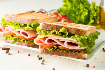 Close-up photo of a club sandwich. Sandwich with meat, prosciutto, salami, salad, vegetables, lettuce, tomato, onion and mustard on a fresh sliced rye bread on wooden background. Olives background.