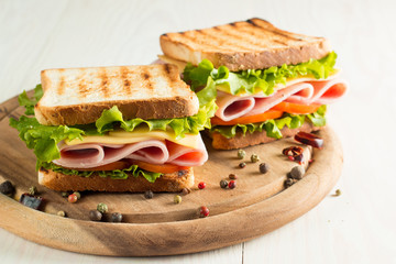 Close-up photo of a club sandwich. Sandwich with meat, prosciutto, salami, salad, vegetables, lettuce, tomato, onion and mustard on a fresh sliced rye bread on wooden background. Olives background.