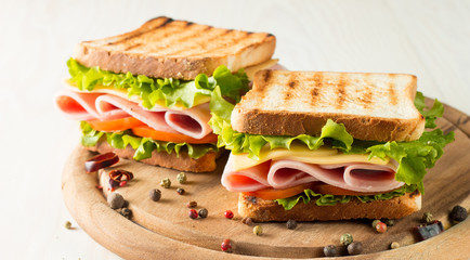 Close-up photo of a club sandwich. Sandwich with meat, prosciutto, salami, salad, vegetables, lettuce, tomato, onion and mustard on a fresh sliced rye bread on wooden background. Olives background.